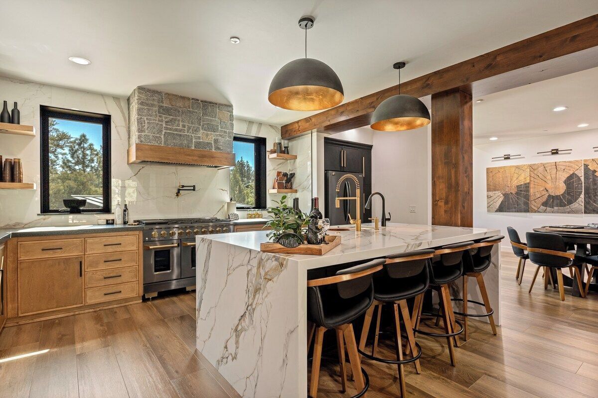 A modern kitchen with a marble island, wooden bar stools, and a stone fireplace.