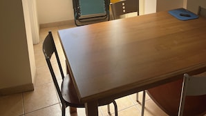 Ein Zimmer mit einem Holztisch, zwei Stühlen, einem Fenster mit gelben Vorhängen und einer Tür.