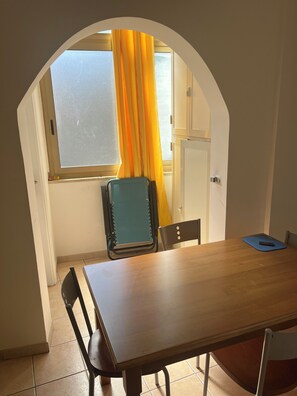 A room with a wooden table, two chairs, a window with yellow curtains, and a door. - Casa di Filippo (Sicilia)