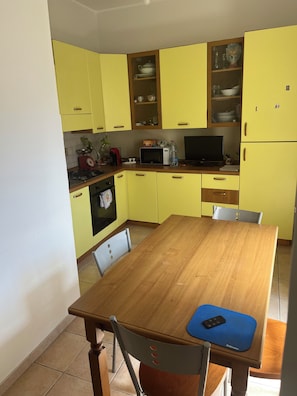 A kitchen with yellow cabinets, a wooden table, and a blue mat. - Casa di Filippo (Sicilia)