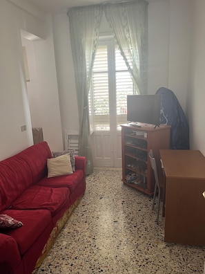 A living room with a red sofa, a wooden cabinet, and a television on a stand. - Casa di Filippo (Sicilia)