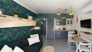 Un espacio habitable moderno con sofá, una mesita redonda, una zona de cocina con microondas y un televisor montado en la pared.