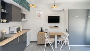Una cocina moderna con microondas, hervidor de agua y un mueble pequeño. Hay un televisor en la pared y un refrigerador.