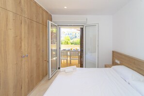 Quarto com cama, armário de madeira e porta de vidro deslizante para área externa com cadeiras e mesa.