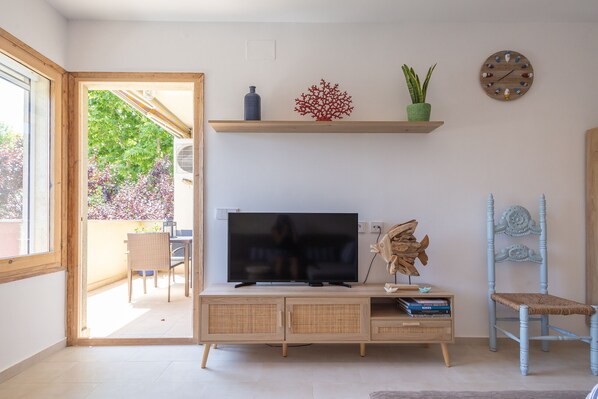 Uma sala de estar com televisão, estantes de madeira, uma cadeira e um vaso de planta.