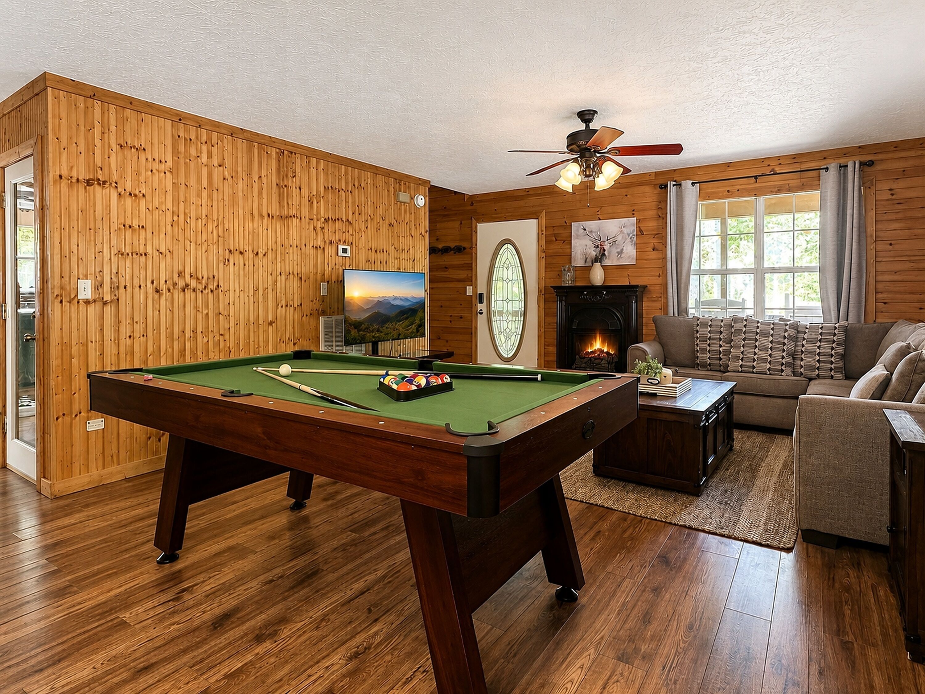 A pool table in a room with wooden walls, a fireplace, and a sofa.