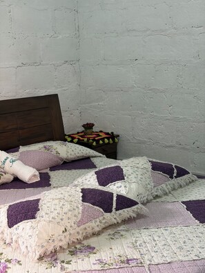 Una cama con colcha estampada, cabecera de madera y mesita de noche con un florero.