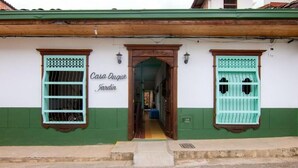 Un edificio con fachada verde y blanca, una puerta de madera y dos ventanas con rejas de metal.