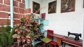 Quarto com parede de tijolos, teto verde, máquina de costura, cadeira vermelha, cadeira verde e estante de livros com livros e uma moldura.