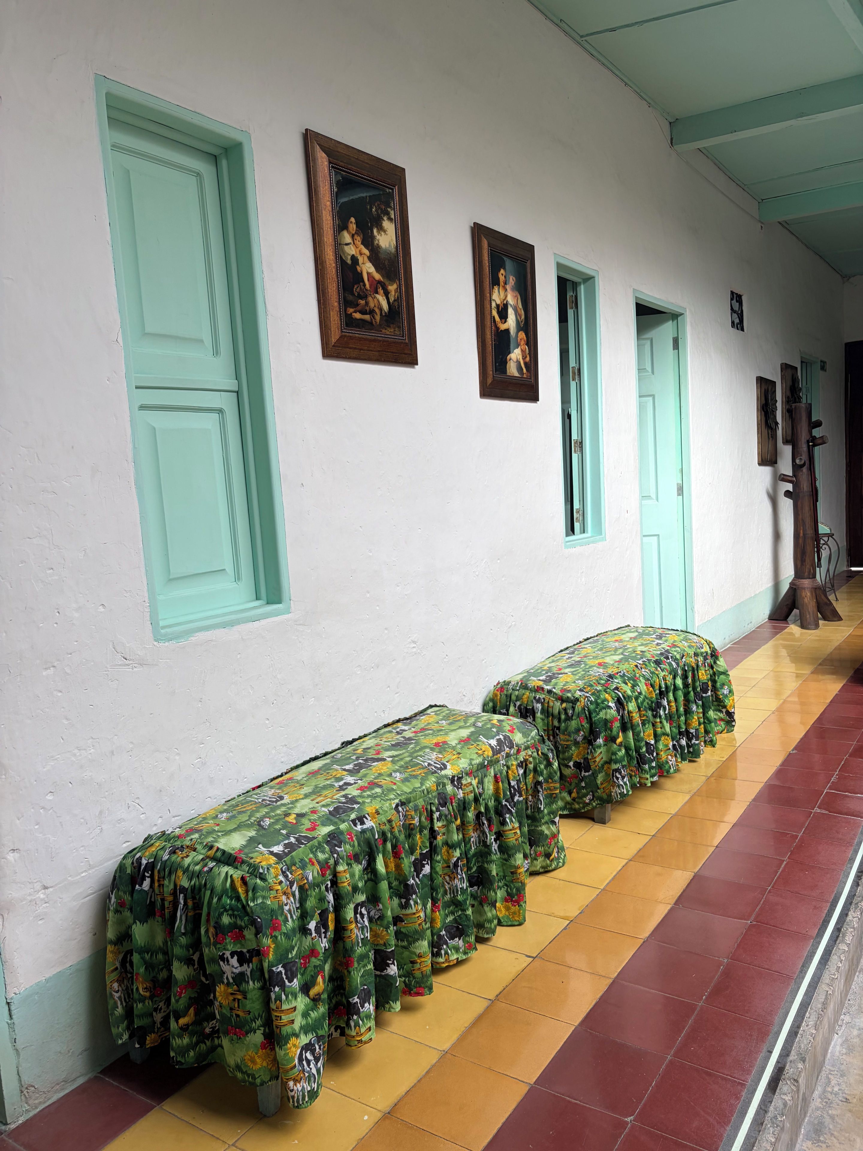 A hallway with a row of benches covered in patterned fabric, a white wall with framed artwork, and doors with teal trim.