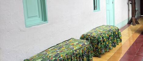 Un pasillo con una fila de bancos tapizados en tela estampada, una pared blanca con obras de arte enmarcadas, y puertas con detalles en color turquesa.