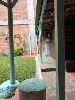 A courtyard with a brick wall, green-painted columns, a grassy area, and a stone bench. - Casa Duque Jardin (Jardín)