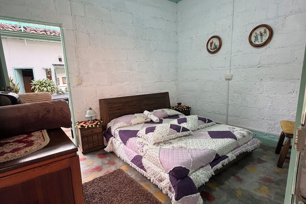 Un dormitorio con cama, cómoda de madera, mesita de noche, espejo y puerta.