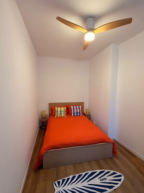 A bedroom with a bed, a ceiling fan, bedside lamps, and a rug.