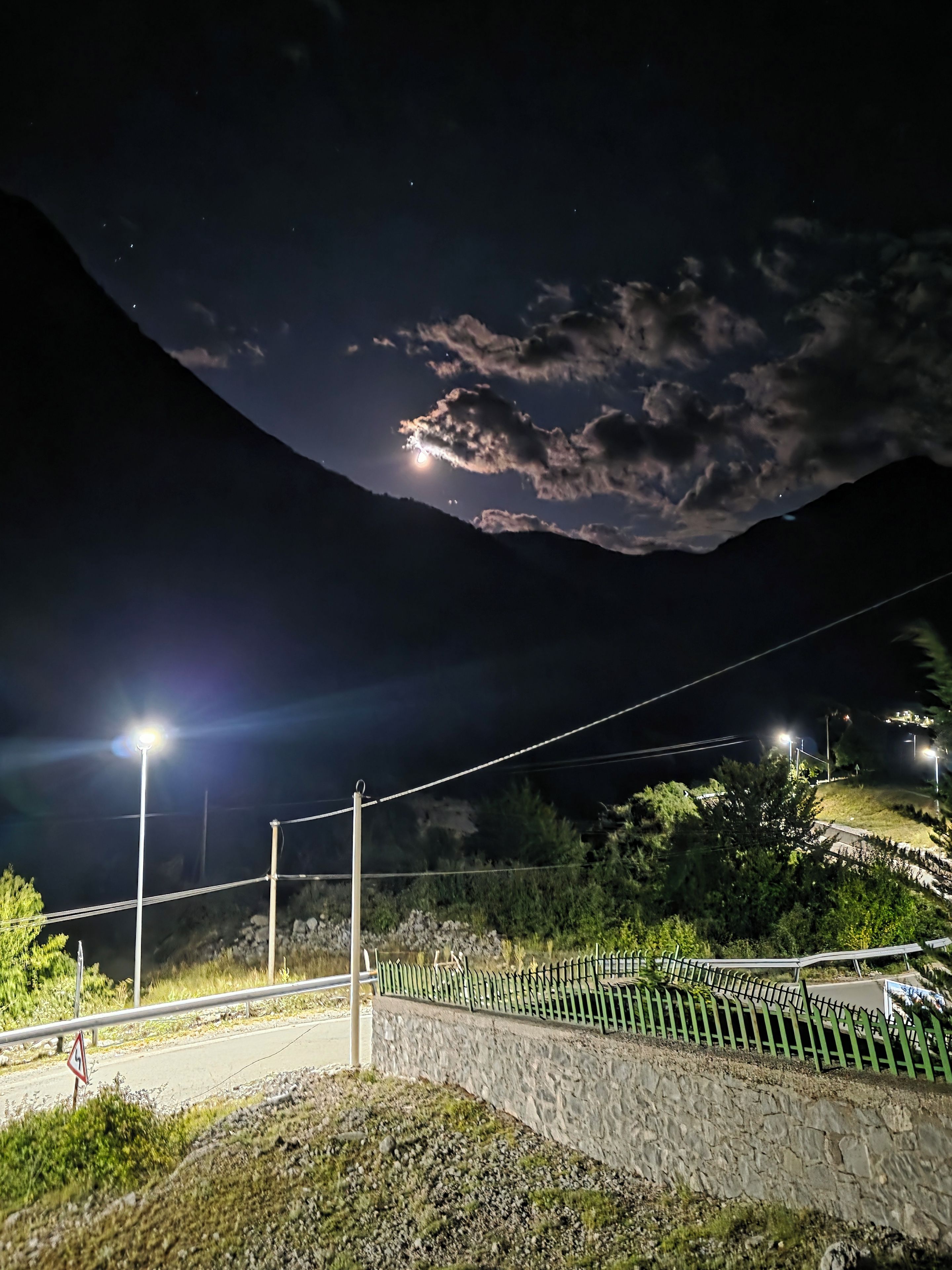 A nighttime view of a mountainous area with a stone wall and a metal fence.