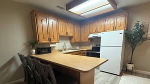 A kitchen with wooden cabinets, a central island with chairs, a refrigerator, and a potted plant. - 1-bedroom apartment with AC near Lake Oroville (Oroville)