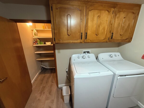 A laundry room with two white washing machines, wooden cabinets above, and a shelf with various items. - 1-bedroom apartment with AC near Lake Oroville (Oroville)