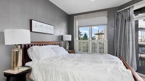 A bedroom with a large bed, two bedside tables, a window with blinds, and a view of the outside. - Wintergreen Ridgeline Retreat (Wintergreen Resort)