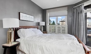 A bedroom with a large bed, two bedside tables, a window with blinds, and a view of the outside. - Wintergreen Ridgeline Retreat (Wintergreen Resort)