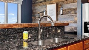 A kitchen with a granite countertop, stainless steel sink, and a wooden backsplash. - Wintergreen Ridgeline Retreat (Wintergreen Resort)
