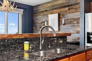 A kitchen with a granite countertop, stainless steel sink, and a wooden backsplash. - Wintergreen Ridgeline Retreat (Wintergreen Resort)