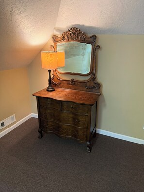A wooden dresser with a mirror and a lamp in a room with beige walls and a sloped ceiling.