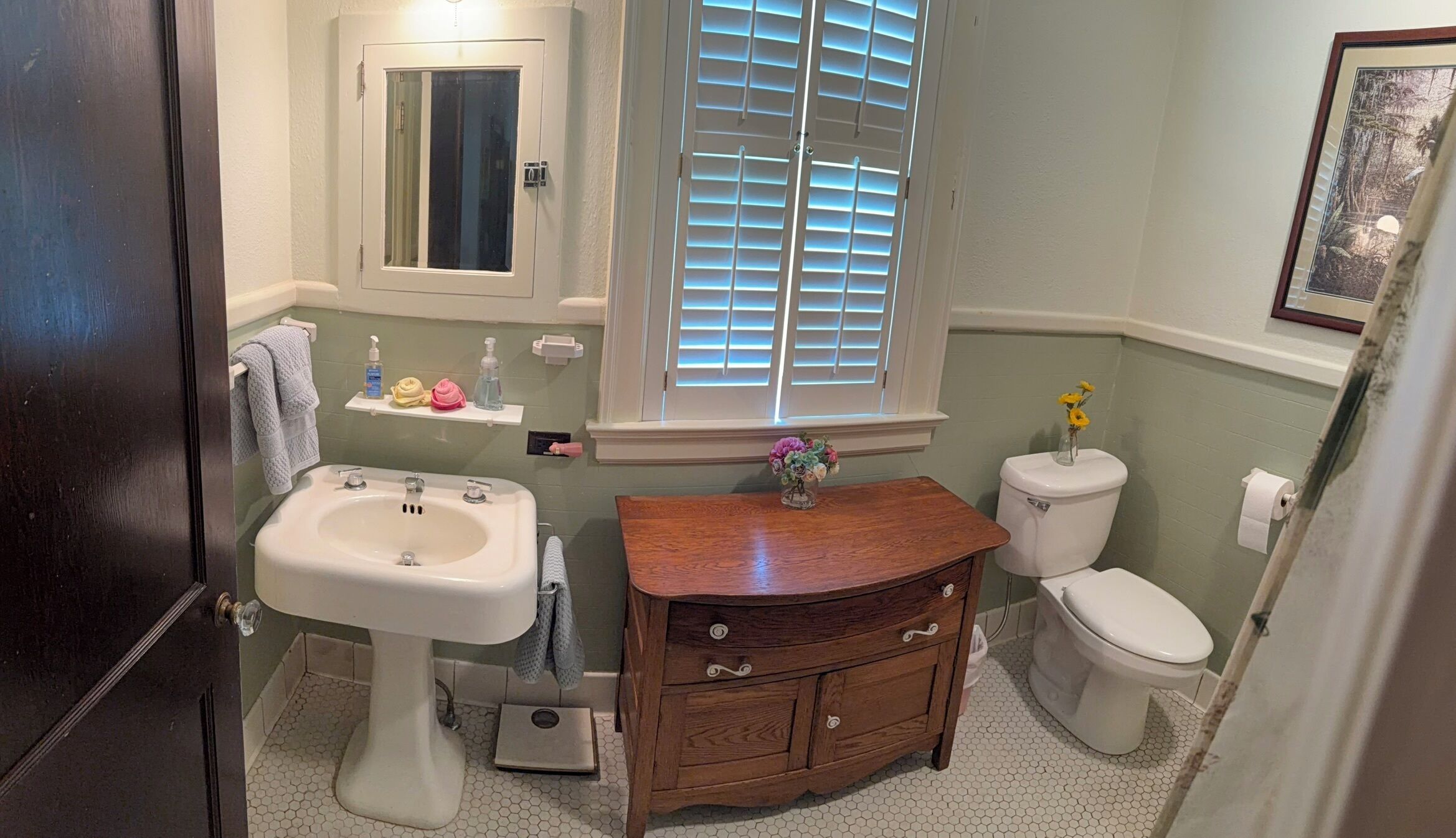 A bathroom with a sink, vanity, toilet, and window with blinds.