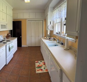 A kitchen with white cabinets, a stove, a sink, and a window with a floral curtain.