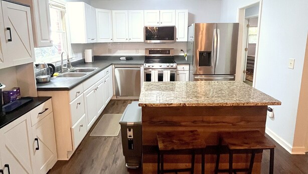 Una cocina moderna con armarios blancos, electrodomésticos de acero inoxidable y una isla central con taburetes de bar.