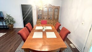 Comedor con mesa de madera, sillas rojas, candelabro y aparador con puertas de vidrio.