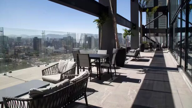 Une terrasse sur le toit avec des sièges extérieurs, une balustrade en verre et une vue sur la ville.