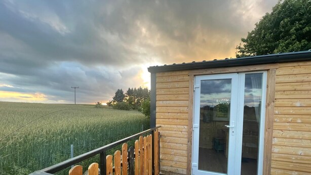 A wooden cabin with a glass door, a metal railing, and a view of a field.