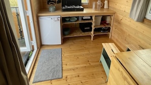 A compact wooden cabin with a kitchenette, a small refrigerator, a window, and a door leading outside.