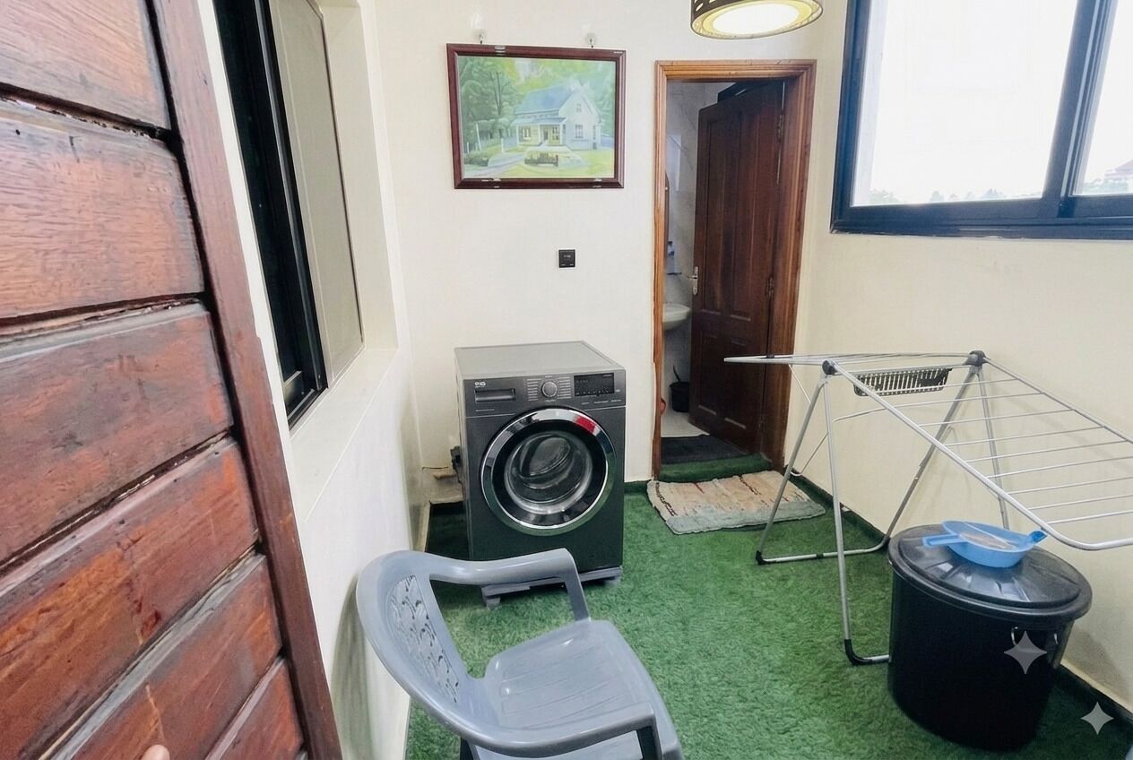 A laundry area with a washing machine, a drying rack, a chair, and a trash bin.