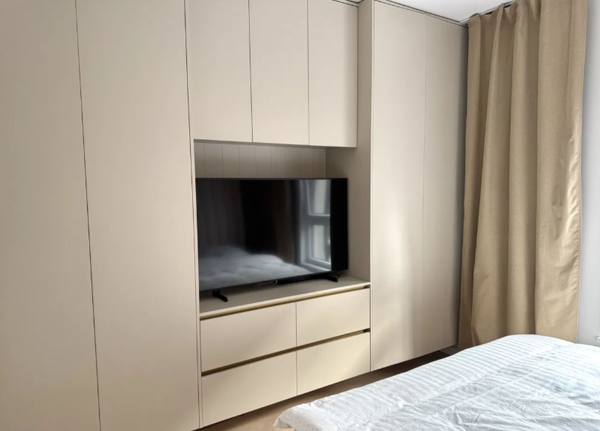 Een slaapkamer met een bed, een aan de muur bevestigde televisie en een kledingkast.