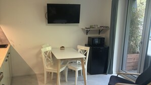 A compact living space with a dining table, chairs, a TV mounted on the wall, a small TV on a stand, and a window with a view of greenery.