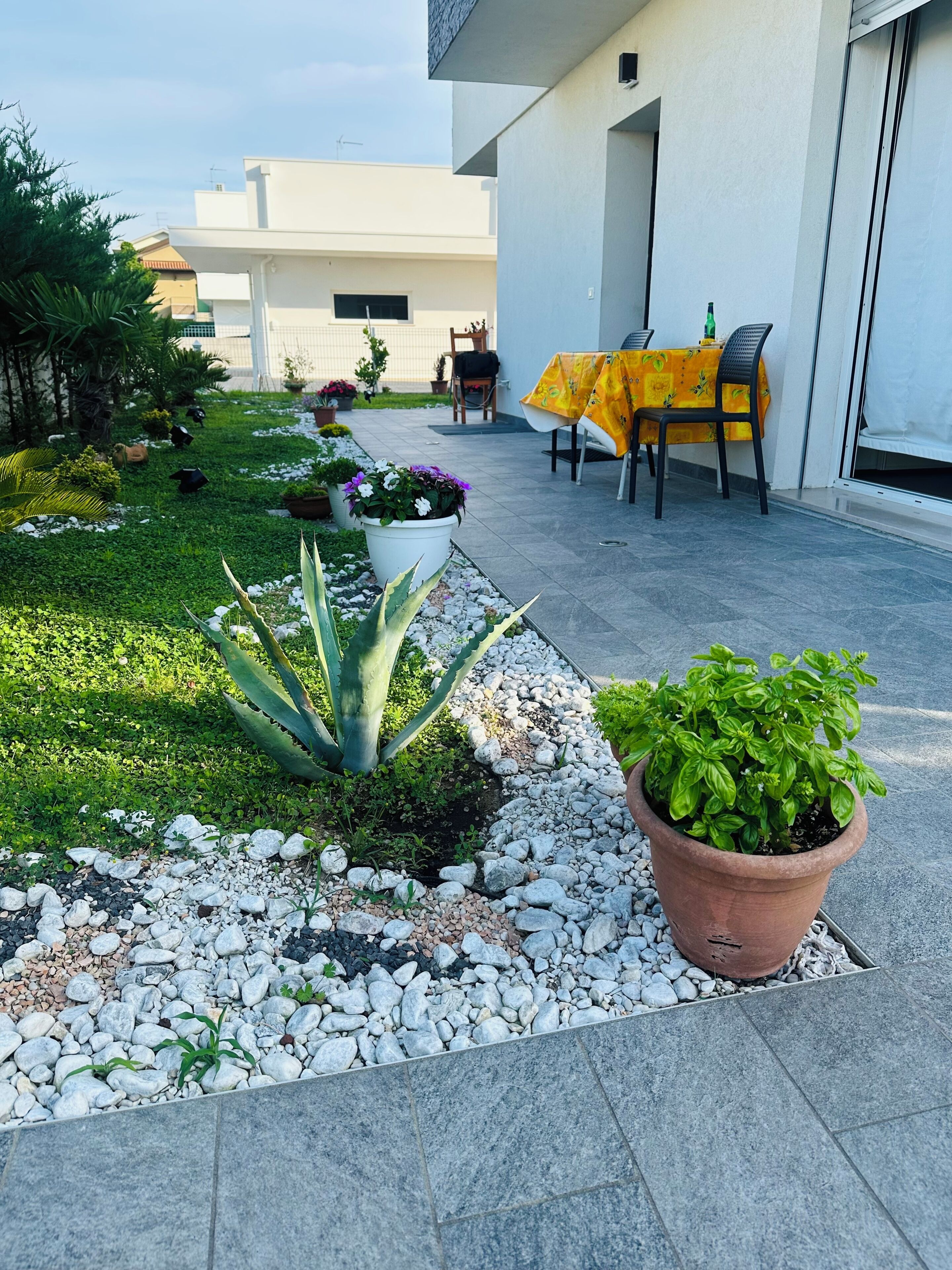 A patio area with a table and chairs, potted plants, and a small garden with rocks and greenery.