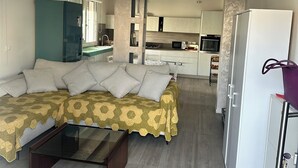 Een moderne woonkamer met een bank, een salontafel, een keuken op de achtergrond en een koelkast.