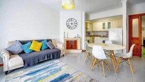 A living room with a sofa, a dining table with chairs, a fireplace, and a kitchen area. - Nazaré - 10 minutes from the ocean (montholon)
