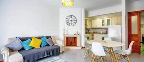 Una sala de estar con sofá, una mesa de comedor con sillas, chimenea y área de cocina.