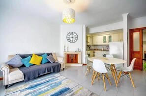 A living room with a sofa, a dining table with chairs, a fireplace, and a kitchen area. - Nazaré - 10 minutes from the ocean (montholon)