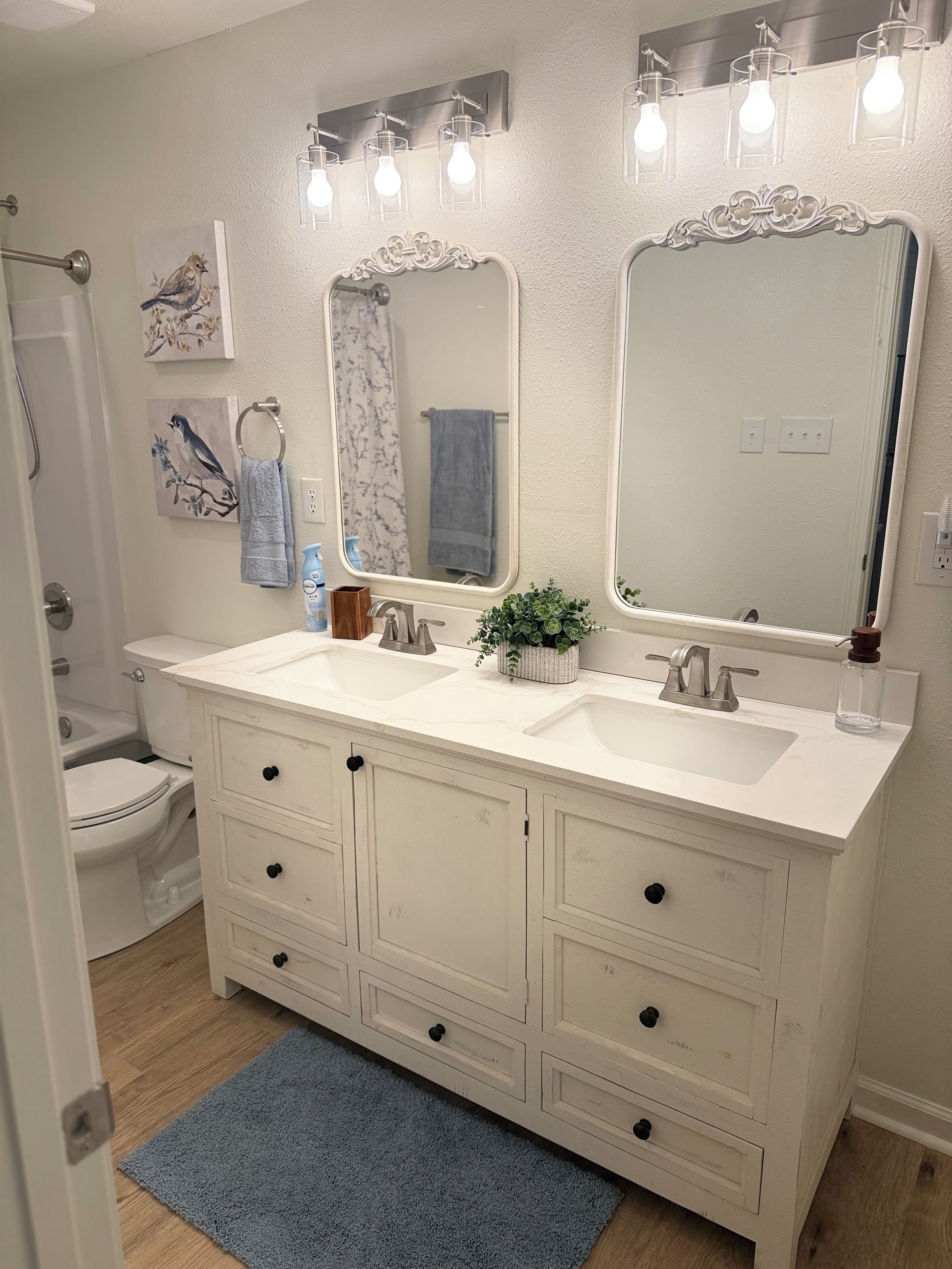 Une salle de bain avec un meuble-lavabo à deux vasques, une douche et des toilettes. Des appliques murales sont fixées au-dessus des miroirs.