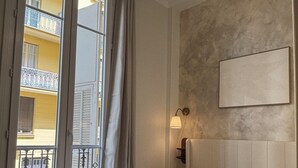 Quarto de hotel com uma cama grande, luminária de cabeceira, vista para uma varanda e um quadro na parede.
