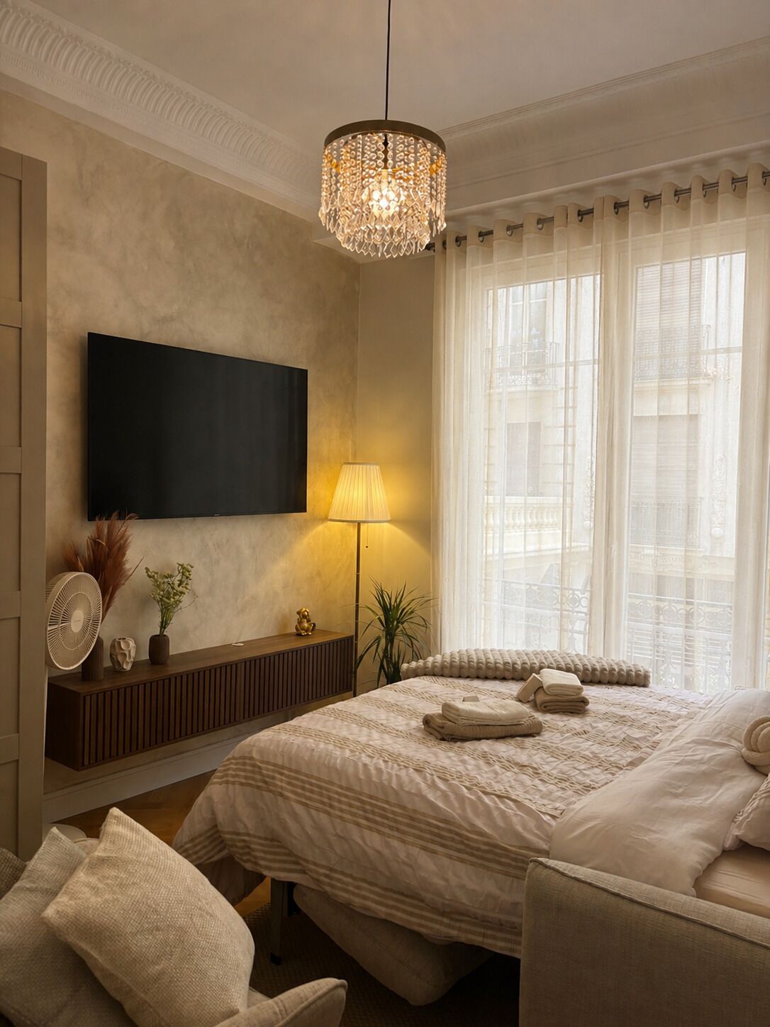 Ein Schlafzimmer mit Bett, Nachttisch, Lampe und einem an der Wand befestigten Fernseher.