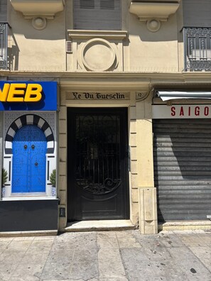 A building facade with a blue door, a sign reading 'Le Du Guesclin,' and a closed shutter to the right. - The Suite des Sables • Spa • Downtown (Nice)