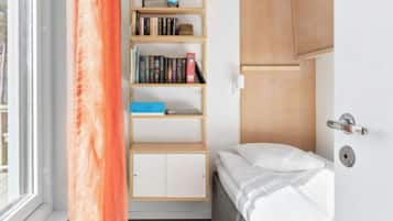 A small, compact room with a bed, a bookshelf, and a window with curtains.