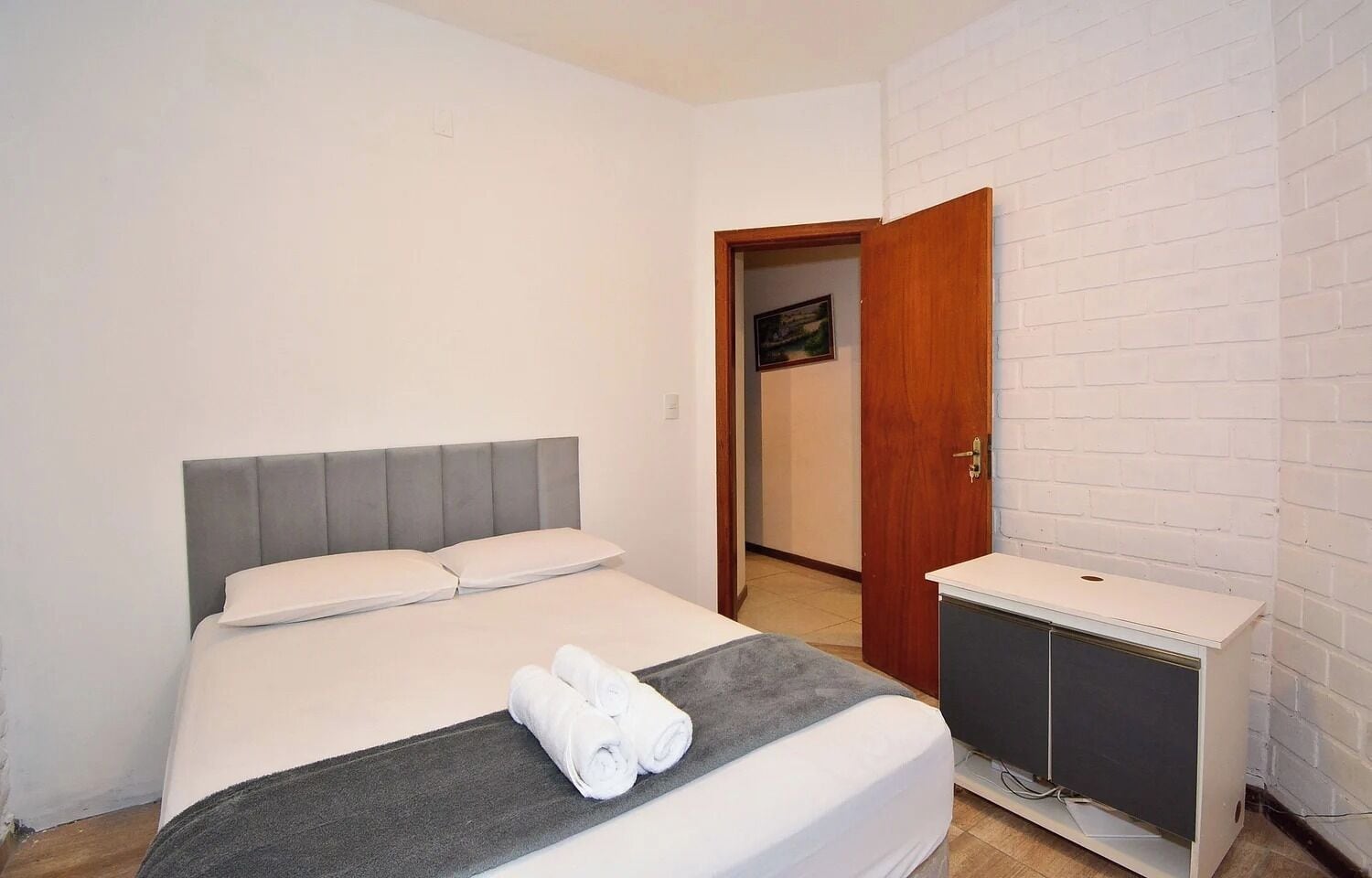Un dormitorio con una cama, una mesita de noche y una puerta que da a otra habitación.