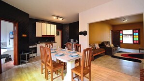 Una cocina moderna con armarios blancos, una mesa de comedor con sillas y una sala de estar con un sofá y una ventana con vidrios de colores.