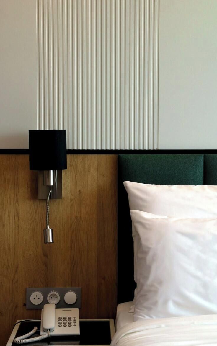 A hotel room with a wooden headboard, a bedside telephone, and a black lamp.