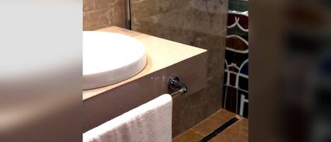 A bathroom with a round sink, a towel hanging on a rack, and a shower area.